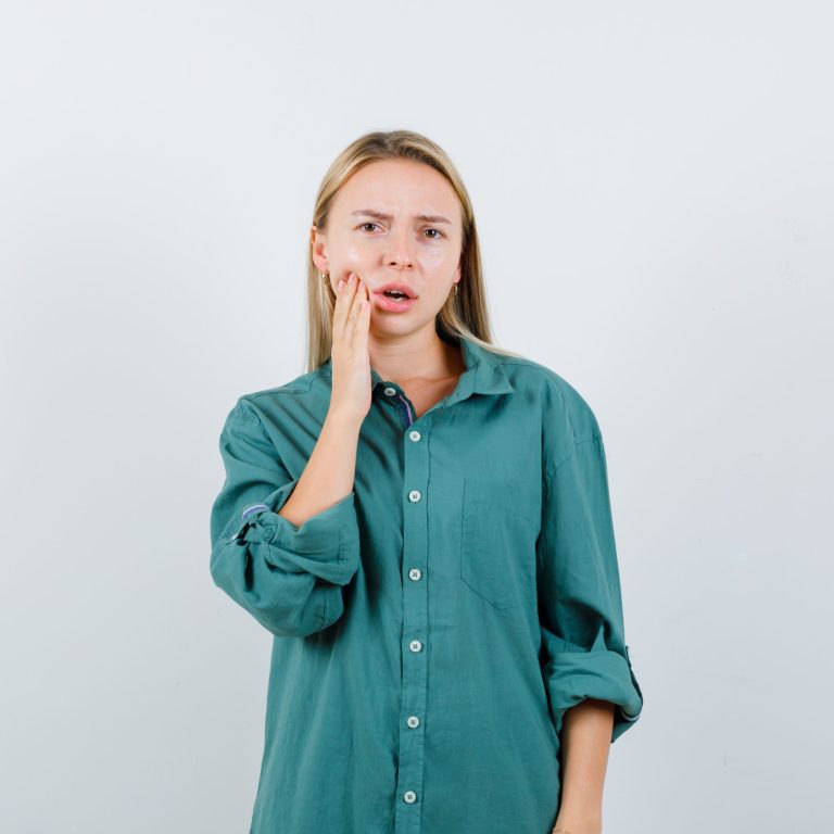 blonde woman suffering from toothache in green shirt and looking uncomfortable , front view.